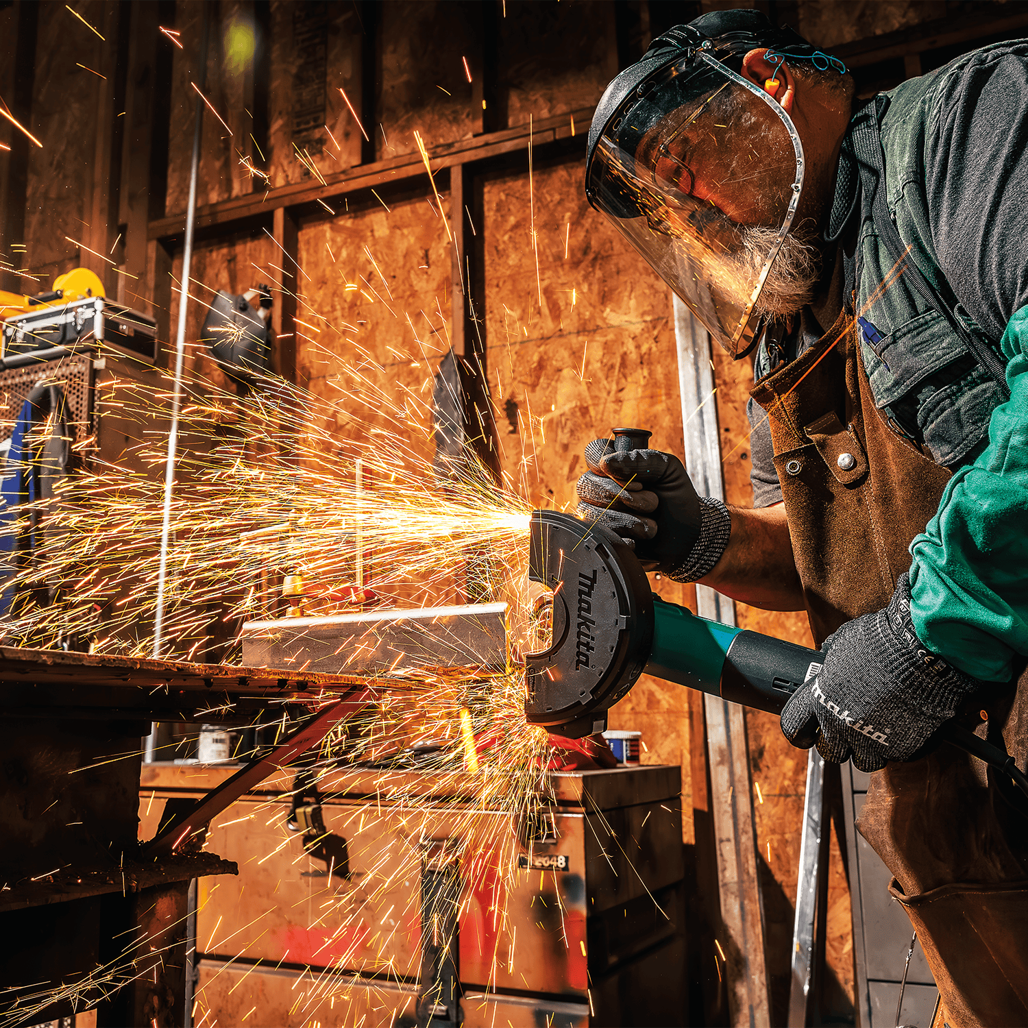 Contractor wearing safety gear using the Makita angle grinder to cut metal tubing, generating a heavy spray of sparks.