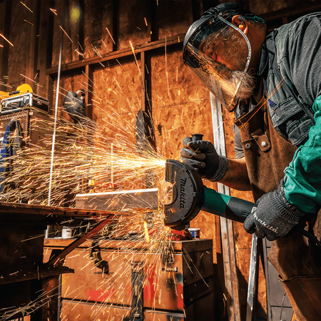 Contractor wearing safety gear using the Makita angle grinder to cut metal tubing, generating a heavy spray of sparks.