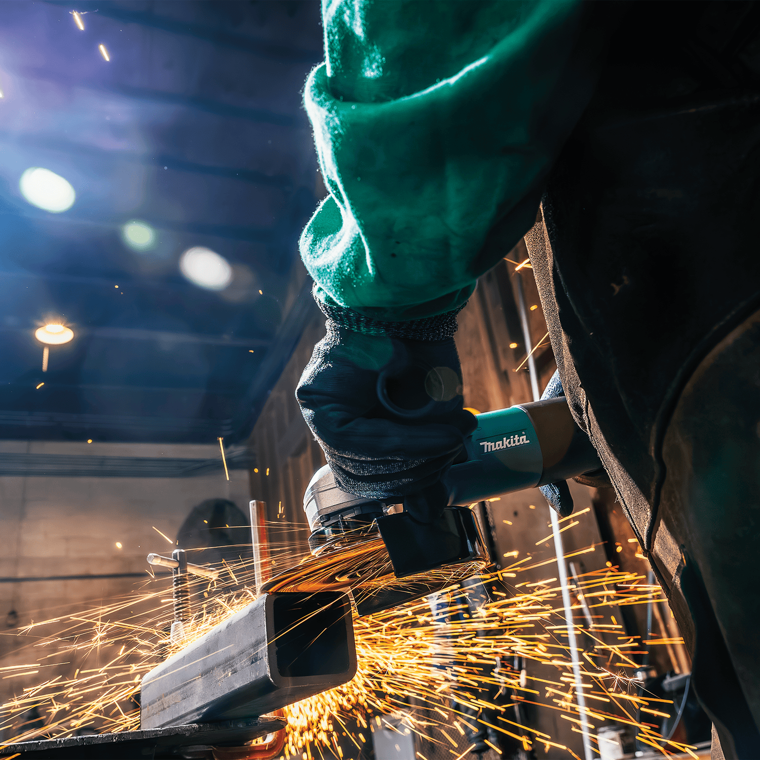 Close-up view of the Makita grinder cutting a square steel tube cleanly while producing bright amber sparks.
