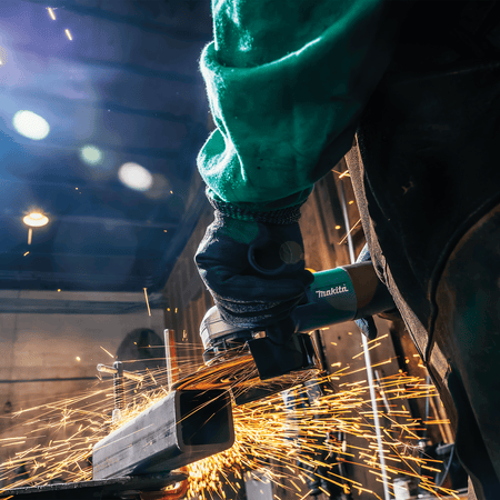 Close-up view of the Makita grinder cutting a square steel tube cleanly while producing bright amber sparks.