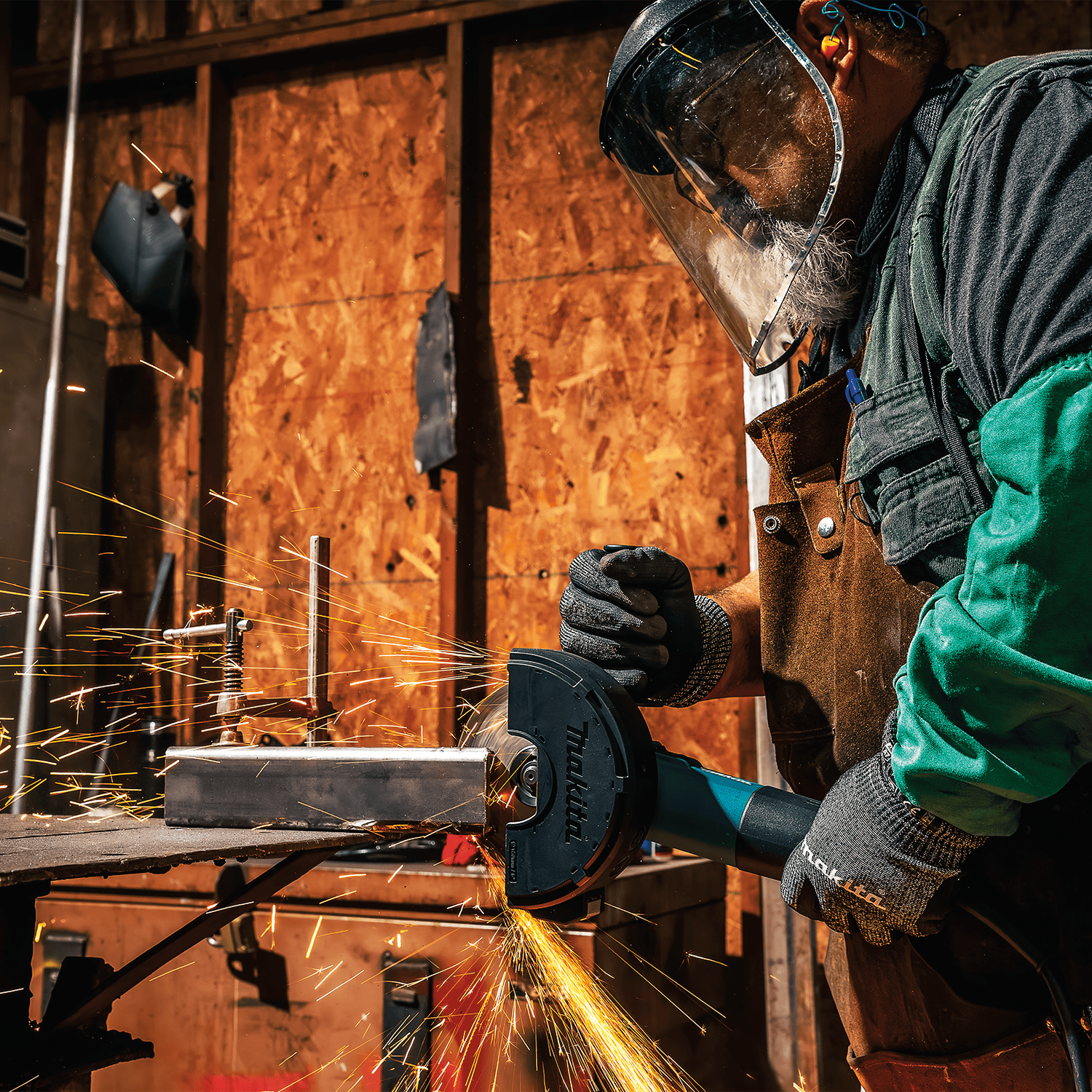Metal fabricator wearing a protective face shield operating the Makita cut-off grinder on a structural steel workpiece.