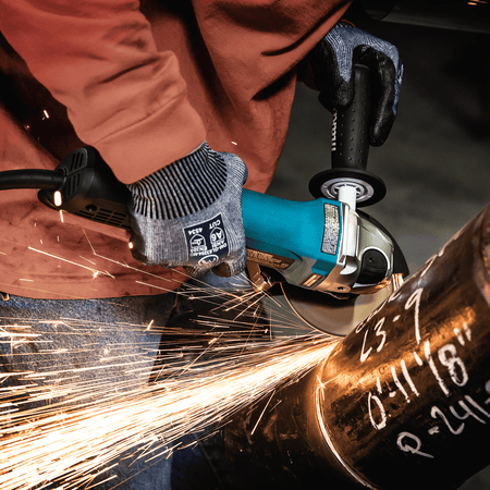 Metal worker beveling a heavy steel pipe seam with the 11.0A Makita GA4553R angle grinder while throwing bright sparks.