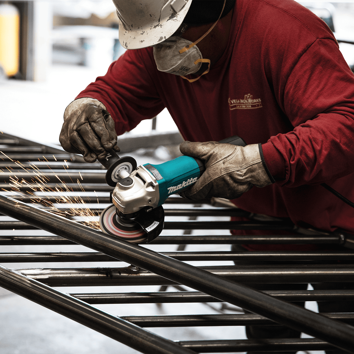 Ironworker using the Makita GA5052 5-inch angle grinder to smooth welds on a steel tubular fence assembly.