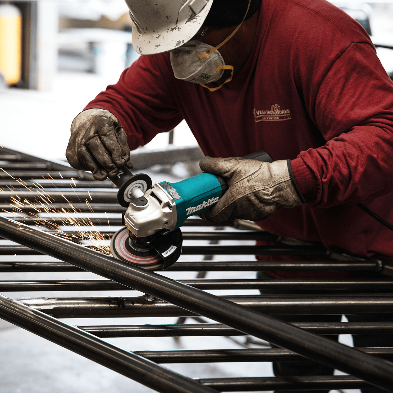 Ironworker using the Makita GA5052 5-inch angle grinder to smooth welds on a steel tubular fence assembly.