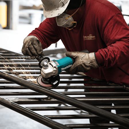 Ironworker using the Makita GA5052 5-inch angle grinder to smooth welds on a steel tubular fence assembly.