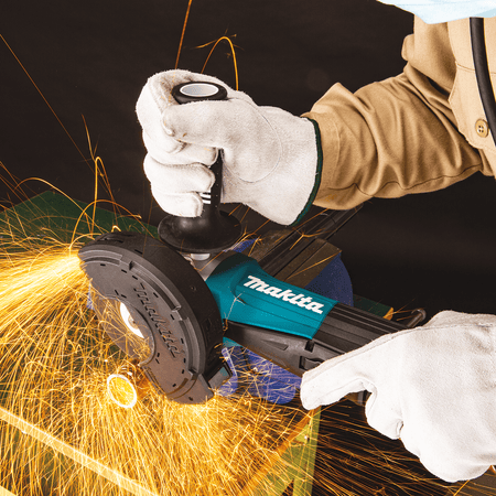Metal fabricator cutting steel conduit with the Makita GA5052 angle grinder fitted with a dust-collecting cutting guard while throwing sparks.