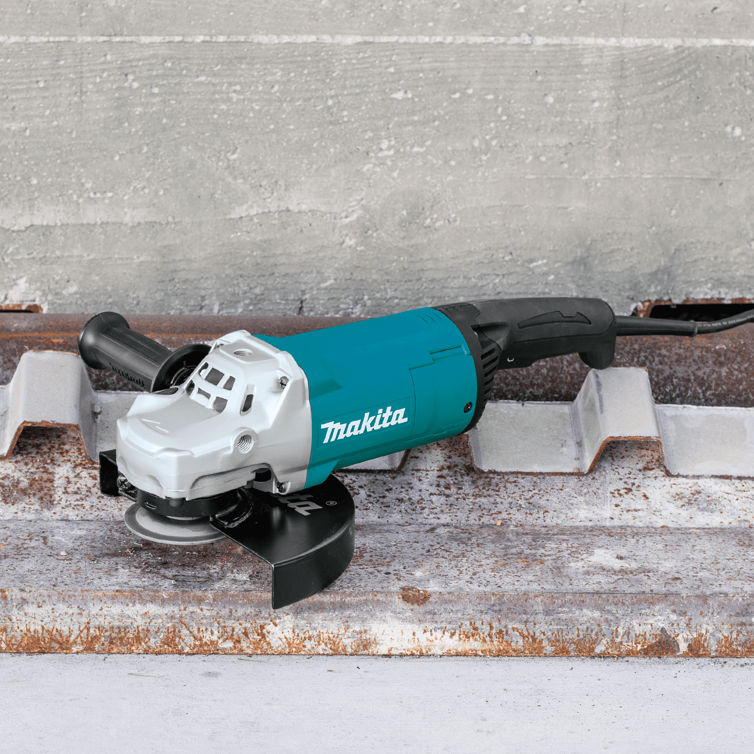 Makita GA9060 9-inch 15.0A corded angle grinder resting on a rusted metal deck plate at an industrial construction site.