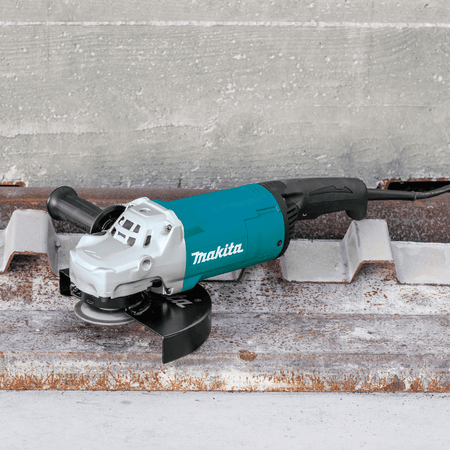 Makita GA9060 9-inch 15.0A corded angle grinder resting on a rusted metal deck plate at an industrial construction site.