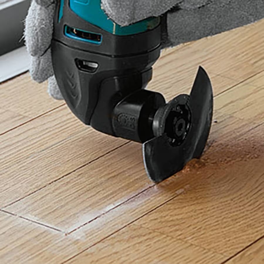 An application shot showing a Makita Starlock oscillating multi-tool performing a precise plunge cut into a hardwood floor, demonstrating clean cutting action.