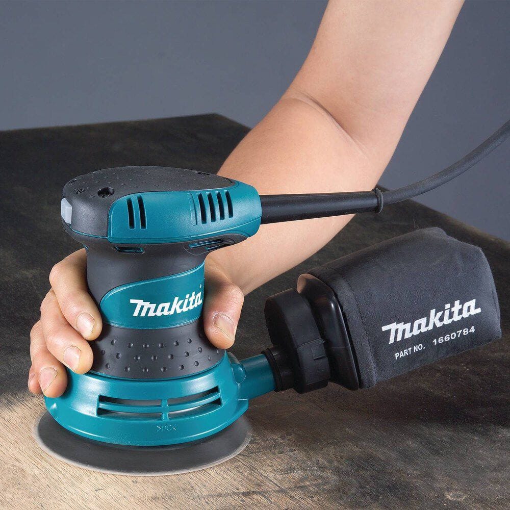 Makita random orbit sander held by a person on a wooden surface