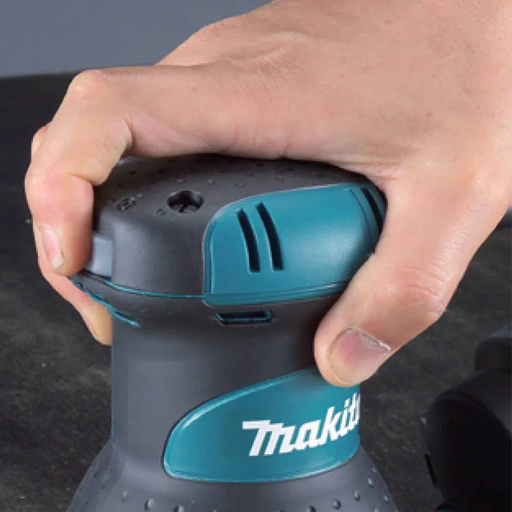 Hand holding a Makita power tool on a dark background