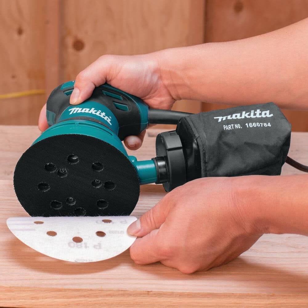 Person using a Makita random orbit sander on a wooden surface