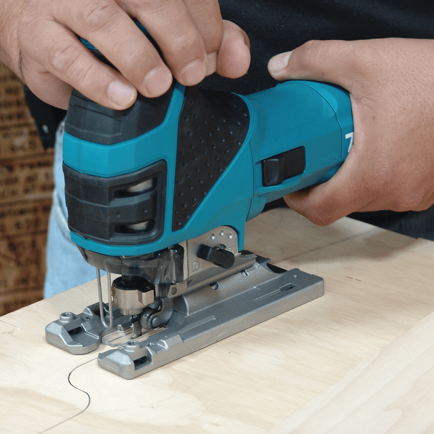 Woodworker guiding a Makita 4351FCT barrel grip jig saw along a curved plywood layout line to demonstrate low-vibration scroll cutting control.