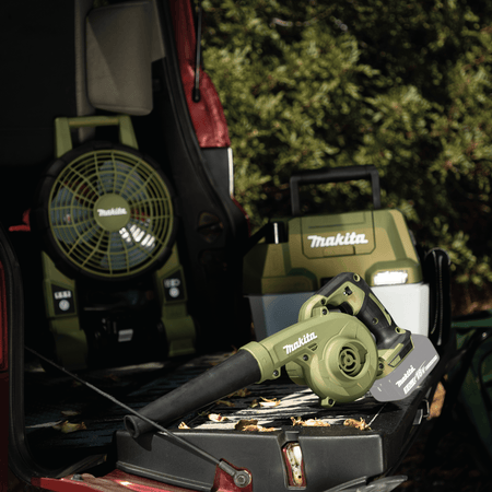 Makita ADBU05Z 18V LXT handheld blower stowed on a vehicle tailgate alongside the Outdoor Adventure fan and wet dry vacuum.