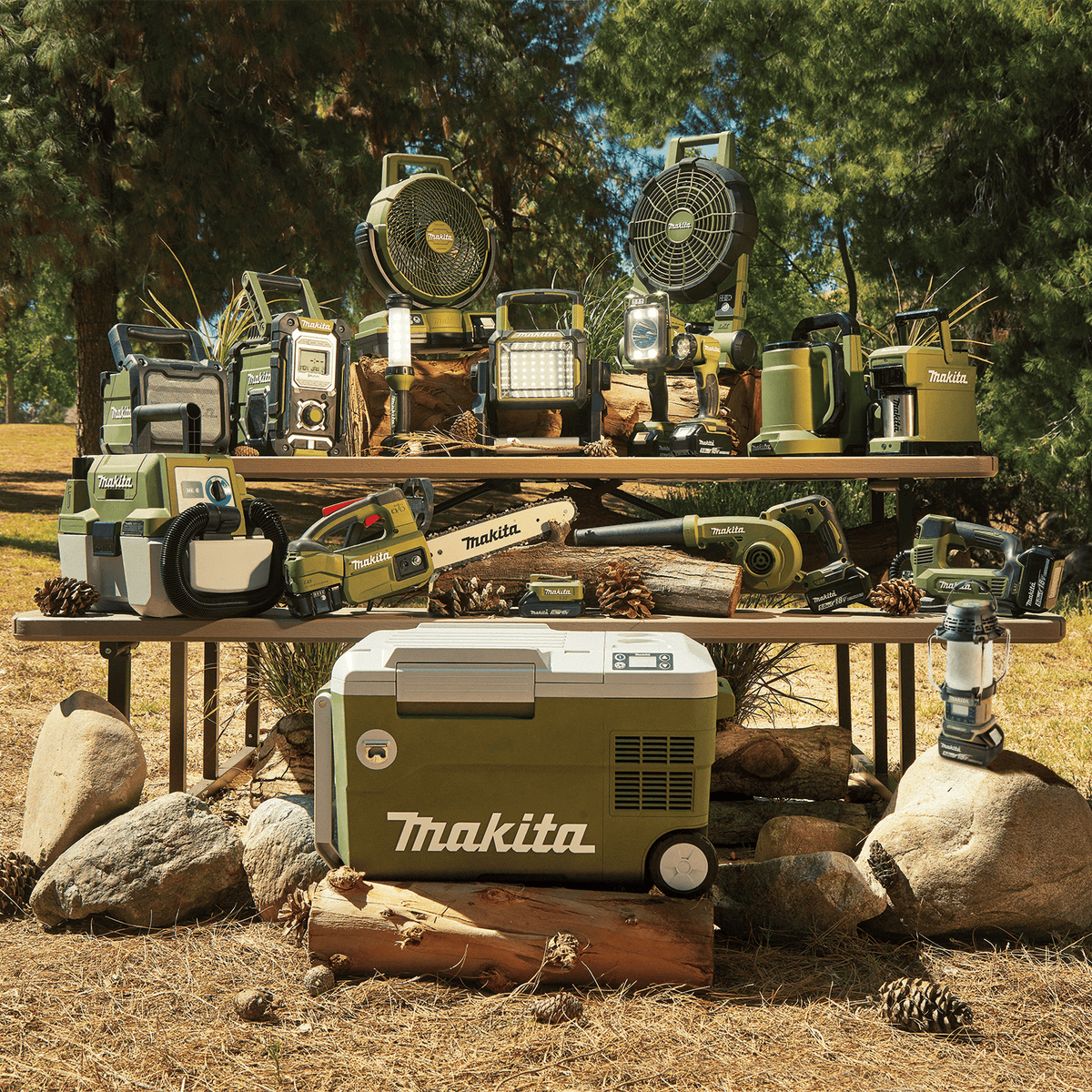 Full Makita Outdoor Adventure 18V LXT lineup on a picnic table featuring the ADBU05Z handheld blower alongside fans, lights, and coolers.