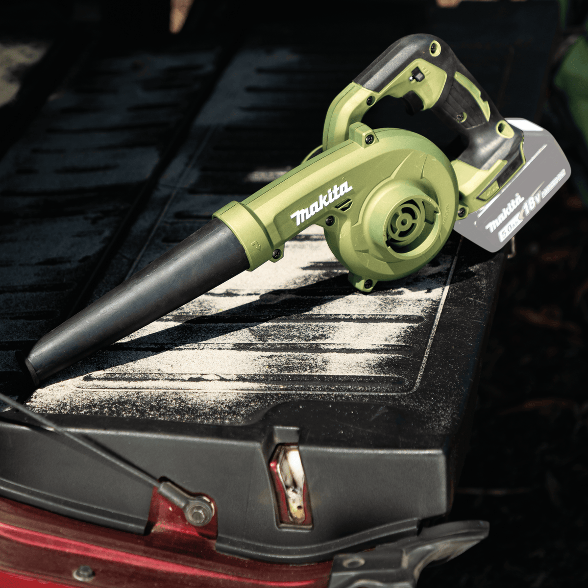 Makita ADBU05Z 18V LXT Outdoor Adventure blower resting on a dusty pickup truck tailgate to demonstrate mobile jobsite bed cleanup.