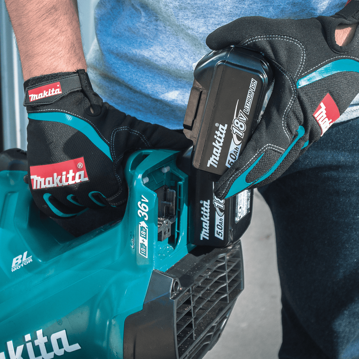 Gloved operator inserting an 18V LXT 5.0Ah battery into the dual battery port of the Makita XBU02 36V brushless handheld blower.