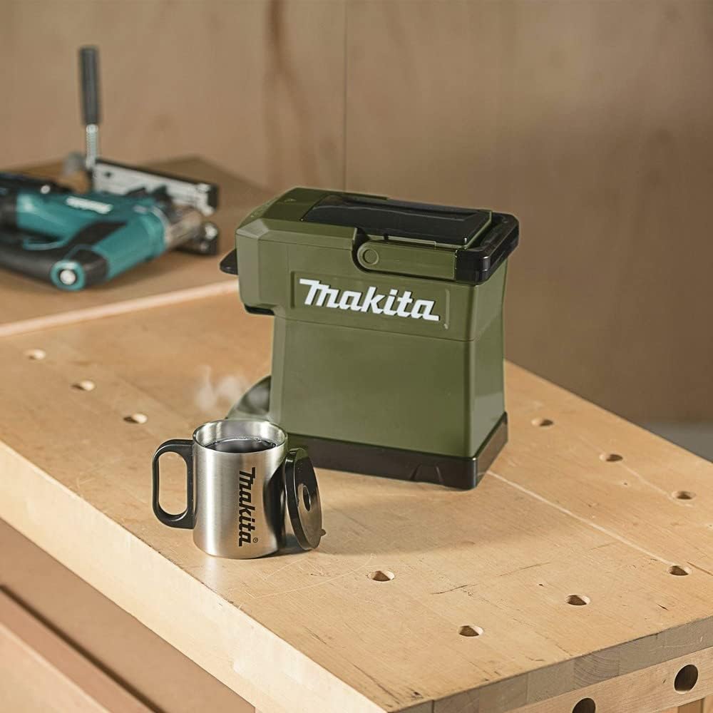 Makita ADCM501Z 18V coffee maker sitting on a woodworking workbench next to a freshly brewed cup of hot coffee in a stainless steel mug.