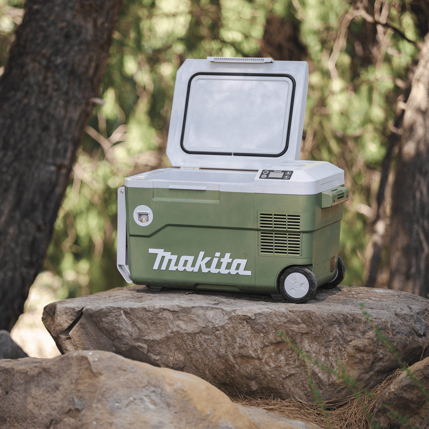 Open Makita ADCW180Z 21-quart cooler resting on a boulder in an outdoor campsite setting showing its insulated storage lid seal.