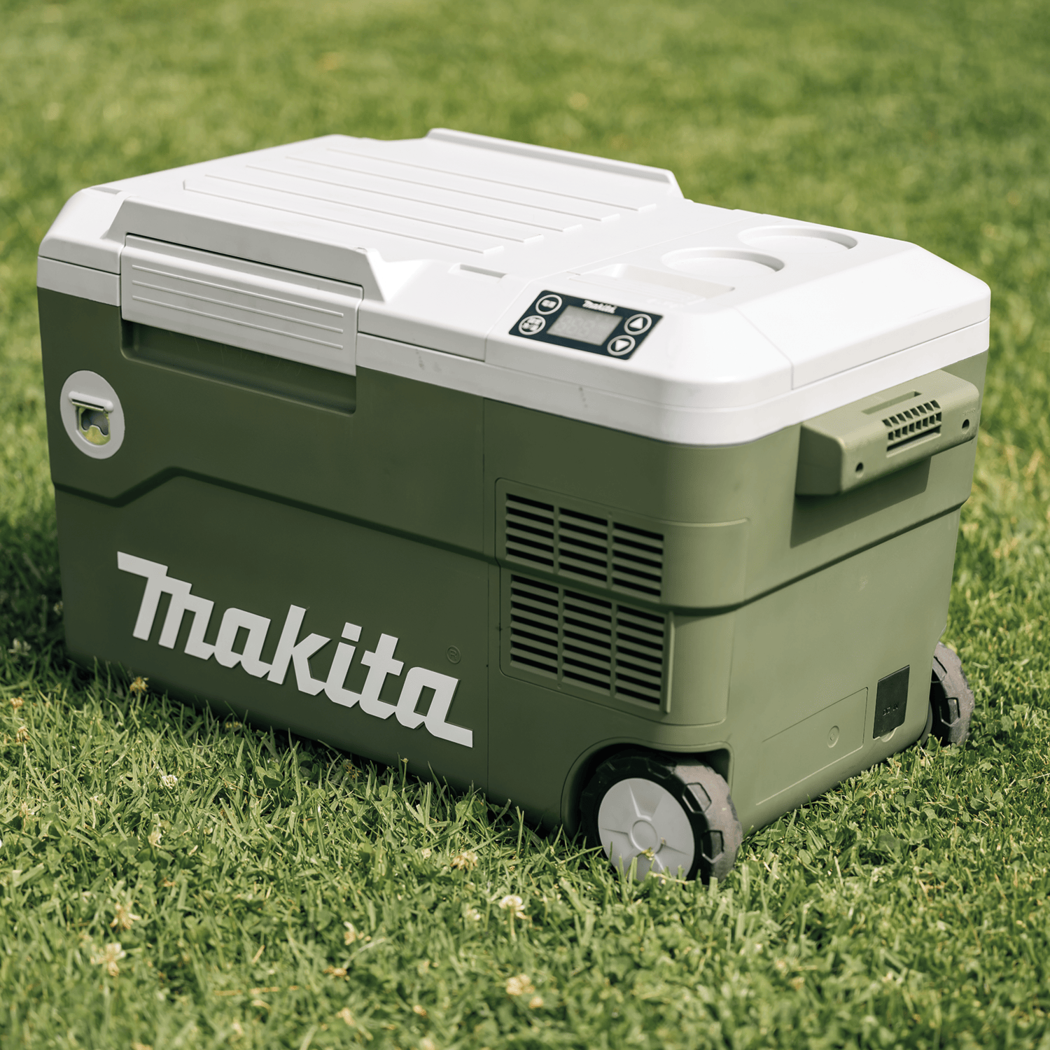 Makita ADCW180Z 18V X2 LXT 21-quart compressor cooler sitting on a green lawn highlighting its rolling wheels and outdoor housing.