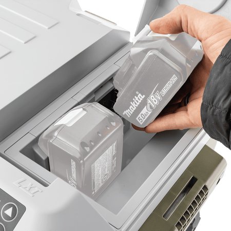 Hand inserting two 18V LXT 5.0Ah lithium-ion batteries into the top weather-sealed battery compartment of the Makita ADCW180Z cooler.