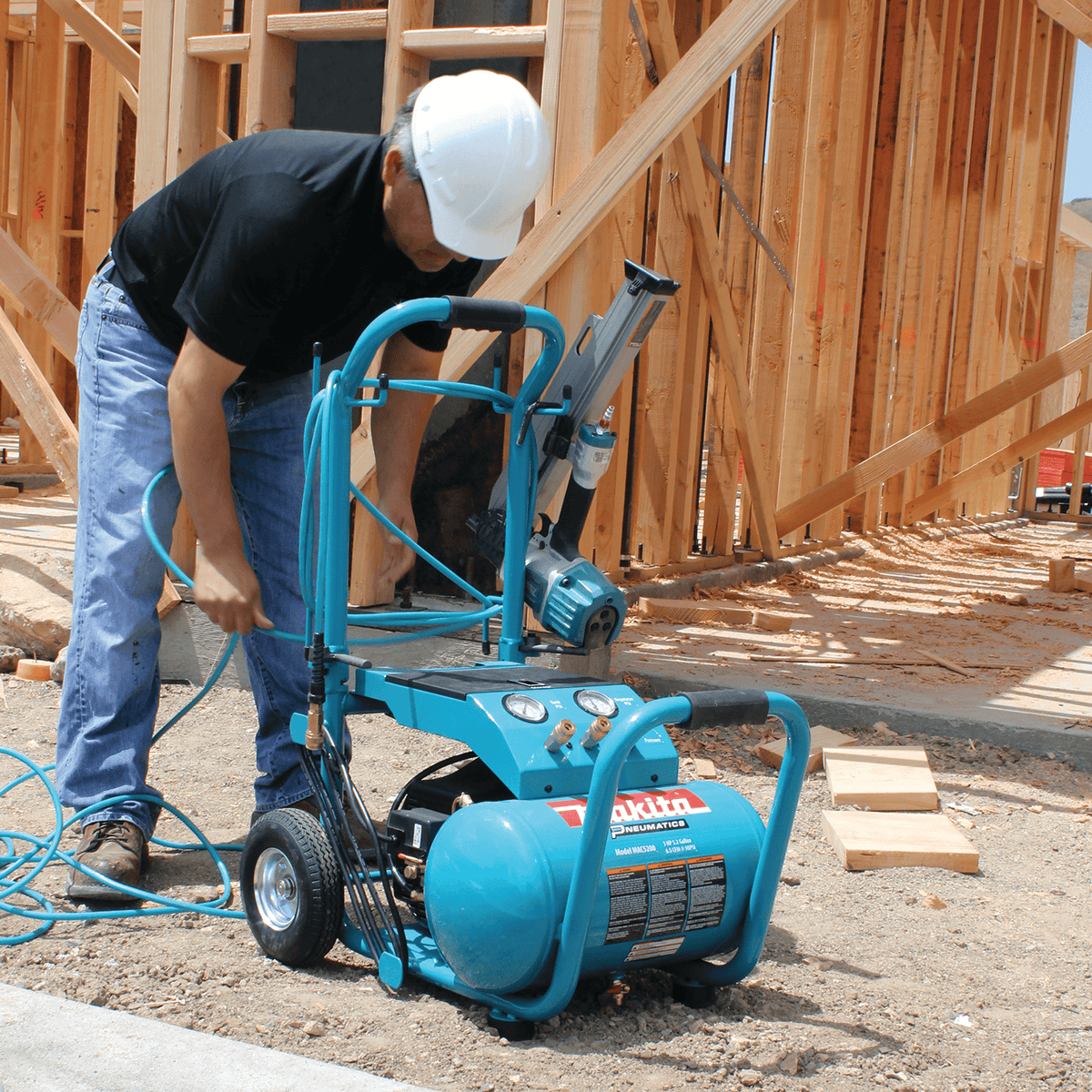 Carpenter connecting an air hose to the Makita MAC5200 5.2-gallon wheeled compressor on a residential framing jobsite.