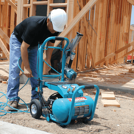 Carpenter connecting an air hose to the Makita MAC5200 5.2-gallon wheeled compressor on a residential framing jobsite.