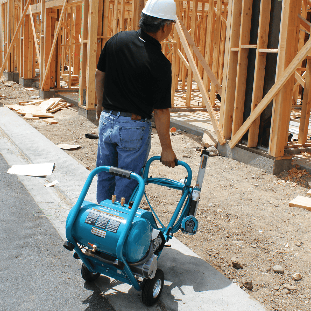 Tradesperson rolling the portable Makita MAC5200 5.2-gallon air compressor across concrete using the rear handle.