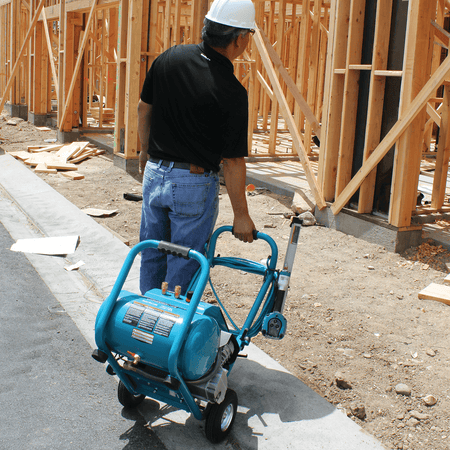 Tradesperson rolling the portable Makita MAC5200 5.2-gallon air compressor across concrete using the rear handle.