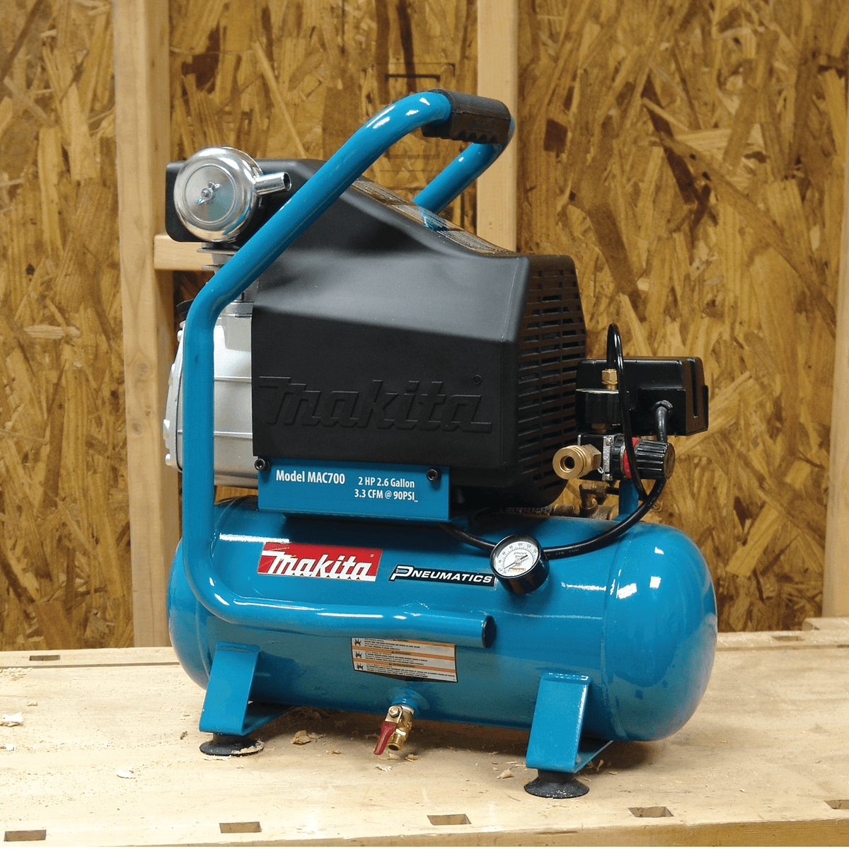 Makita MAC700 2.6-gallon electric air compressor on a workbench showing pressure gauge and quick coupler.