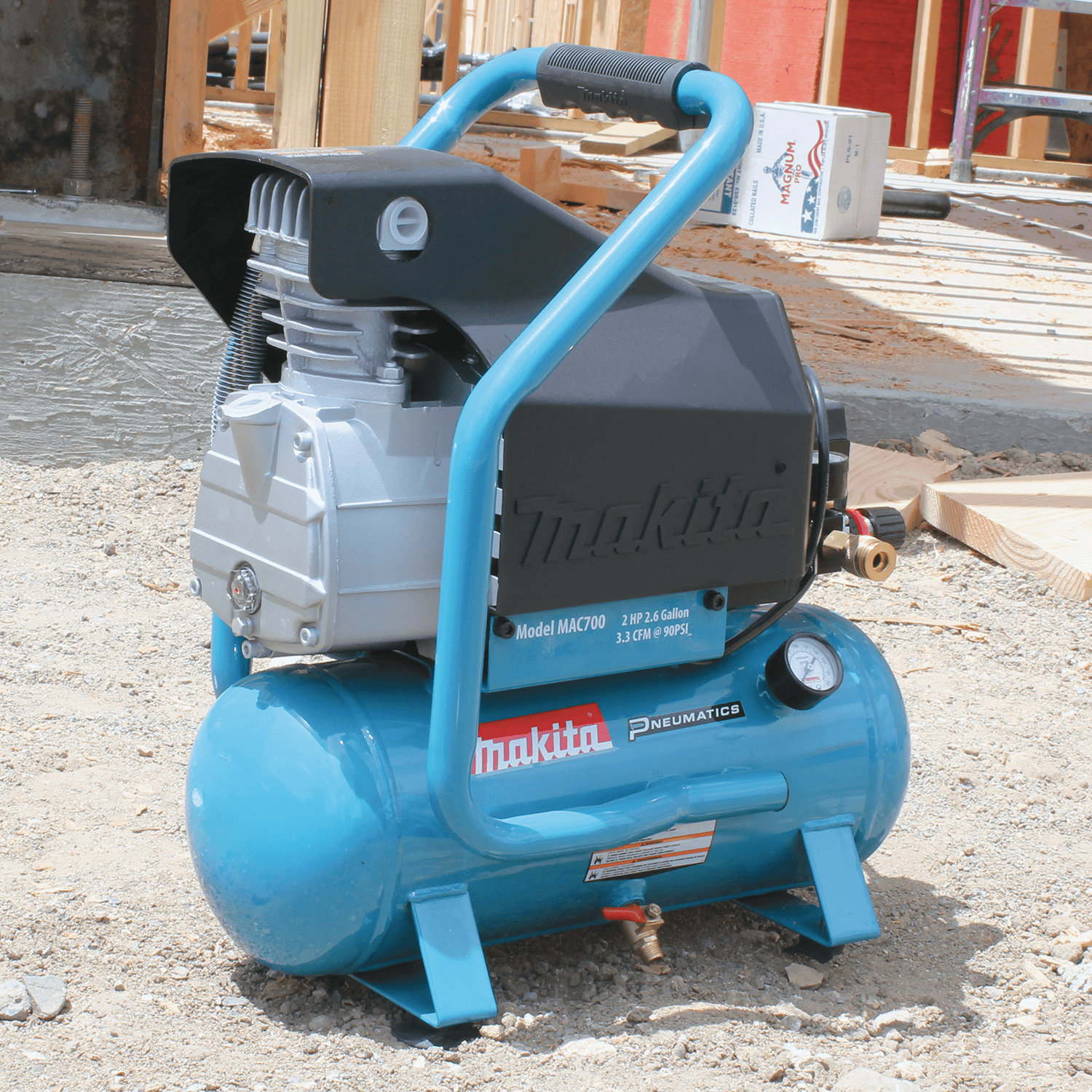Makita MAC700 2.0 HP air compressor on a gravel framing jobsite displaying cast iron pump and brass drain valve.
