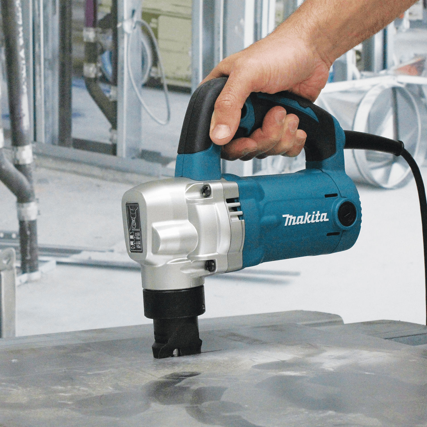 Metalworker making a straight cut through heavy steel plate using the Makita JN3201 corded nibbler on a jobsite prep table.