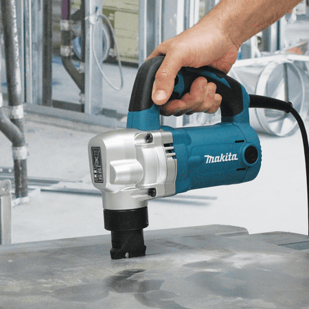 Metalworker making a straight cut through heavy steel plate using the Makita JN3201 corded nibbler on a jobsite prep table.