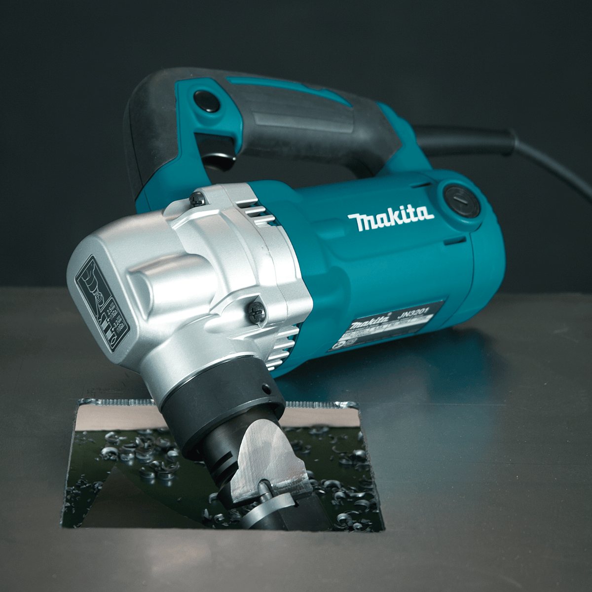 Makita JN3201 10-gauge nibbler completing a square internal cutout in sheet metal showing downward chip disposal beneath the work surface.