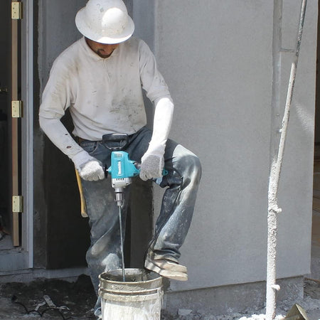 Plasterer using the Makita DS4012 spade handle drill with a paddle attachment to mix stucco compound inside a 5-gallon bucket.