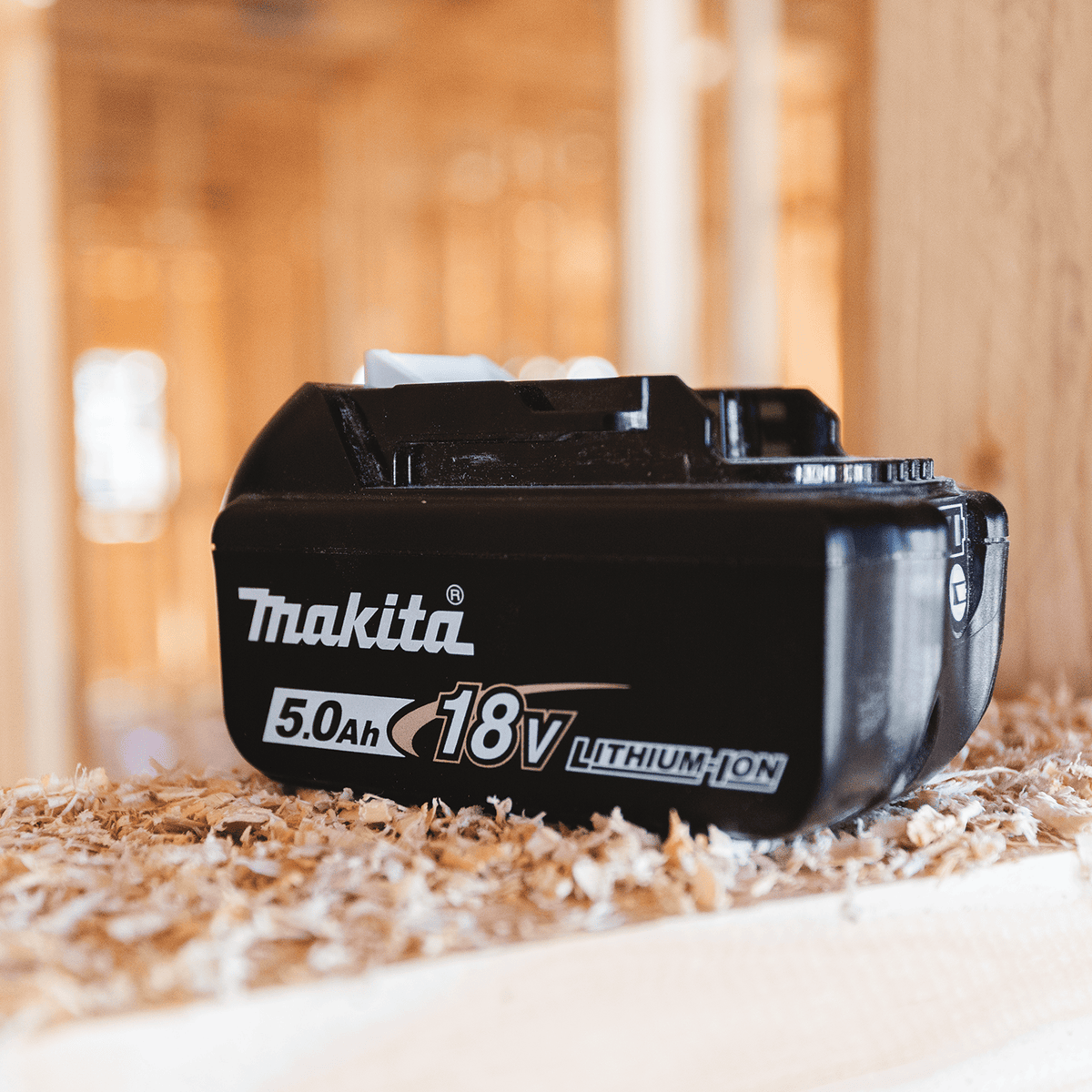 Makita BL1850B 18V 5.0Ah battery resting on a wood framing stud on an active residential construction jobsite.