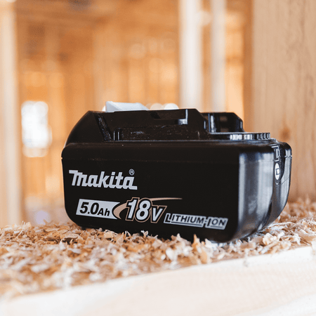 Makita BL1850B 18V 5.0Ah battery resting on a wood framing stud on an active residential construction jobsite.