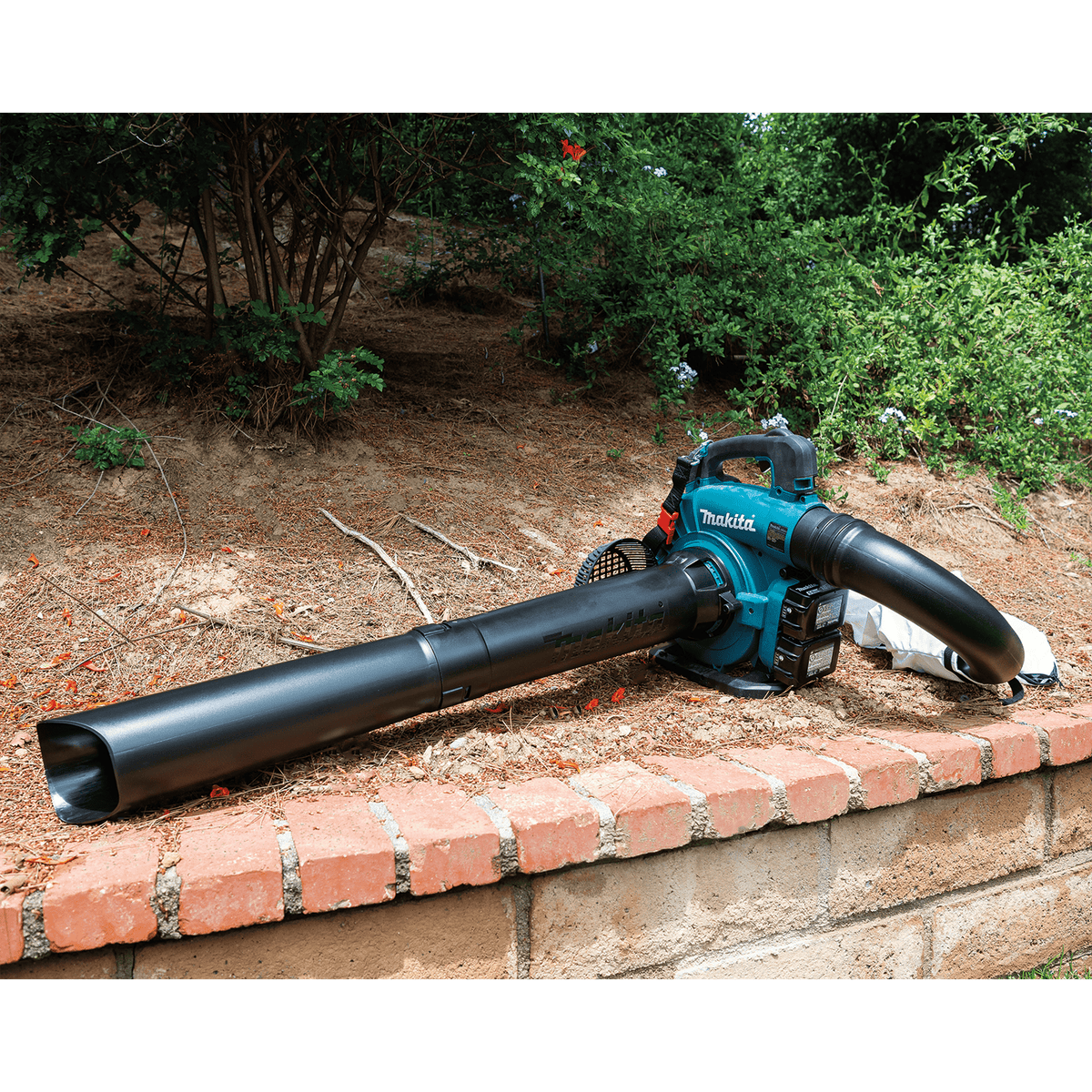 Makita XBU04PTV set up in vacuum and mulcher configuration resting near garden landscaping and brick wall.