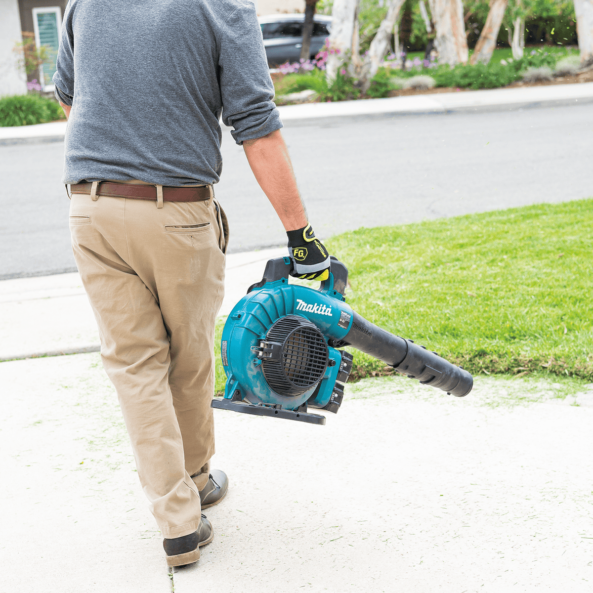Worker carrying the Makita cordless blower comfortably by its handle across a residential lawn.