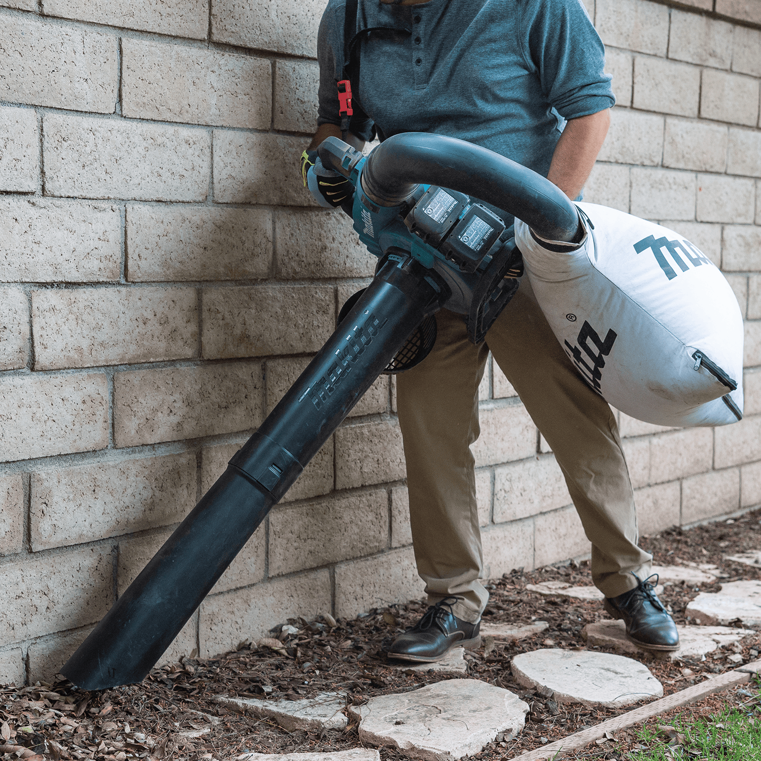 Operator vacuuming leaves near a block wall using the Makita cordless blower and bag setup.