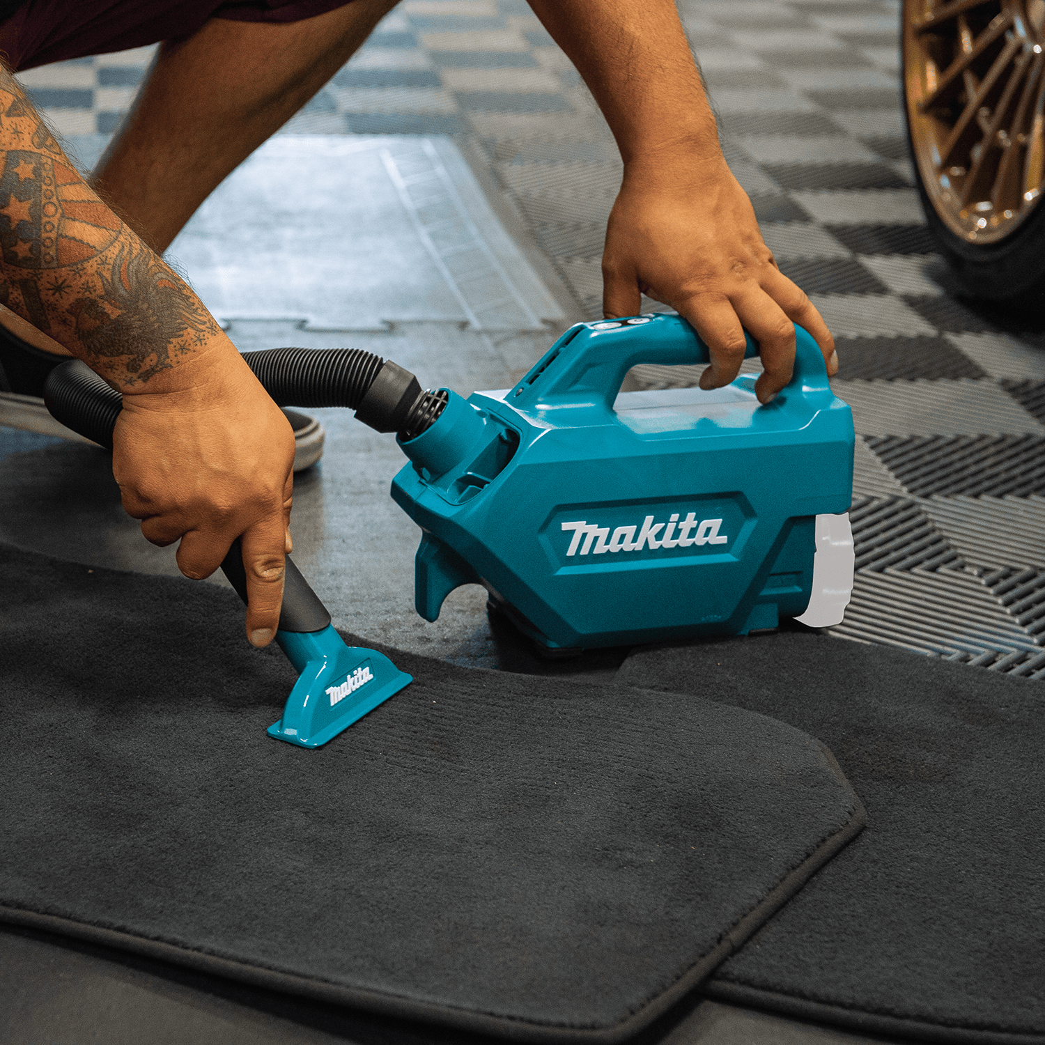 Operator using the Makita XLC07Z cordless canister vacuum with a wide nozzle to clean dirt and debris off a rubber car floor mat.