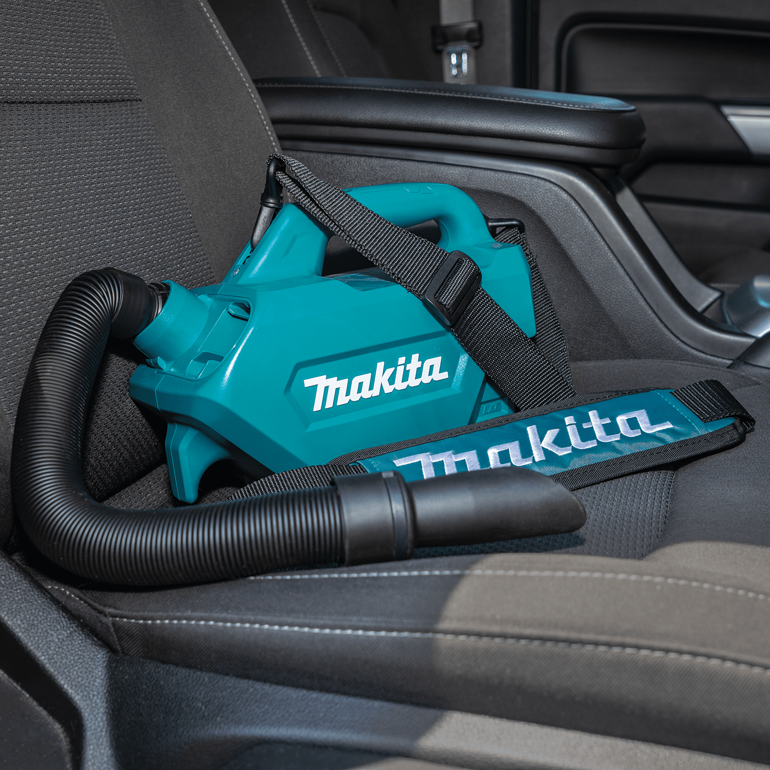 Makita XLC07Z 18V cordless vacuum resting on a car passenger seat with its padded shoulder strap, ready for vehicle cabin maintenance.