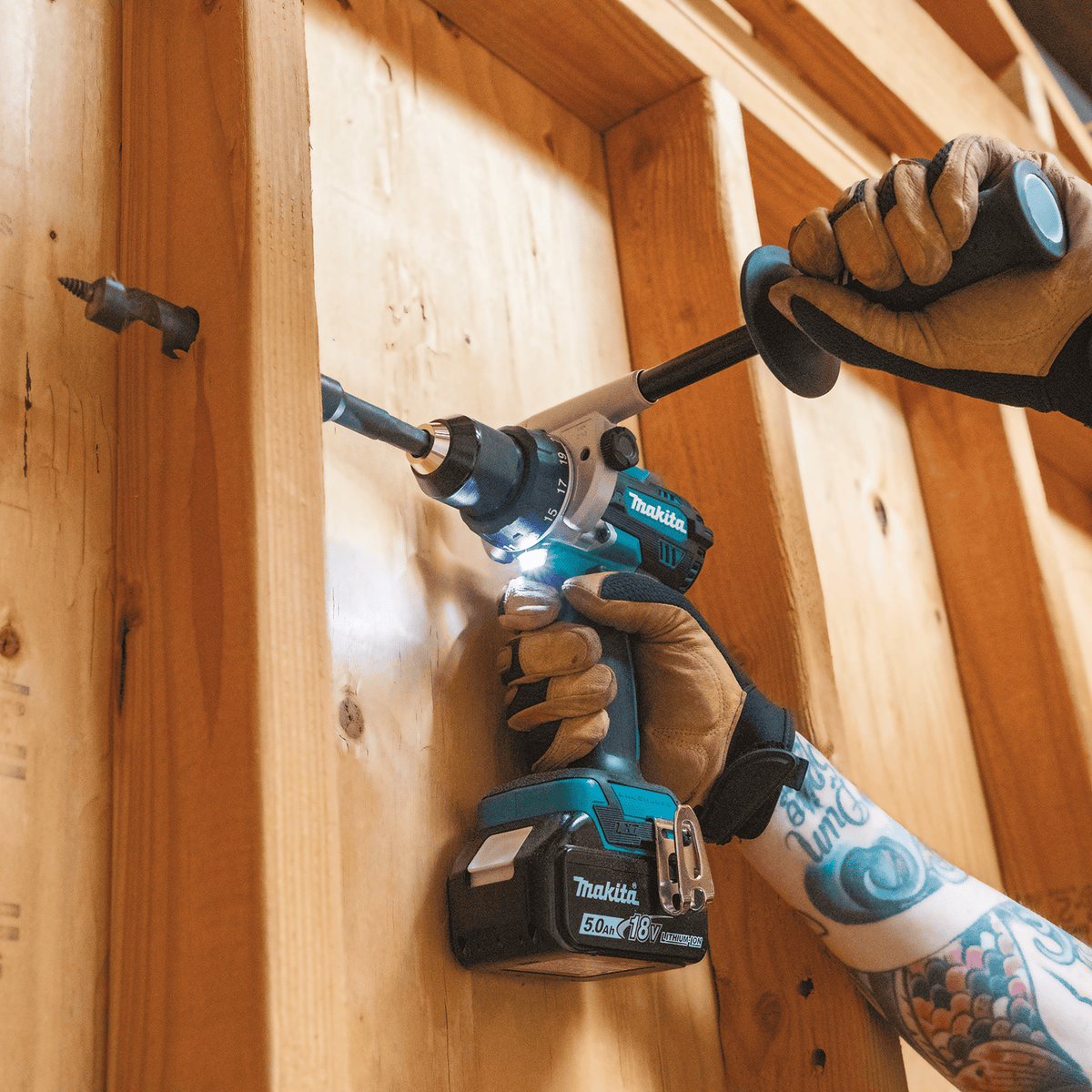 Contractor using the Makita XPH14 18V hammer drill with side handle to bore a pilot hole through a vertical 2x4 wood framing stud.