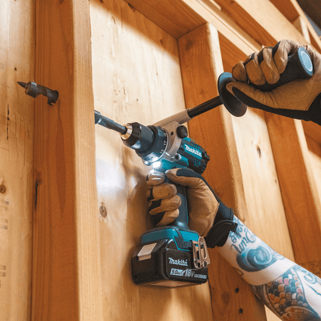 Contractor using the Makita XPH14 18V hammer drill with side handle to bore a pilot hole through a vertical 2x4 wood framing stud.