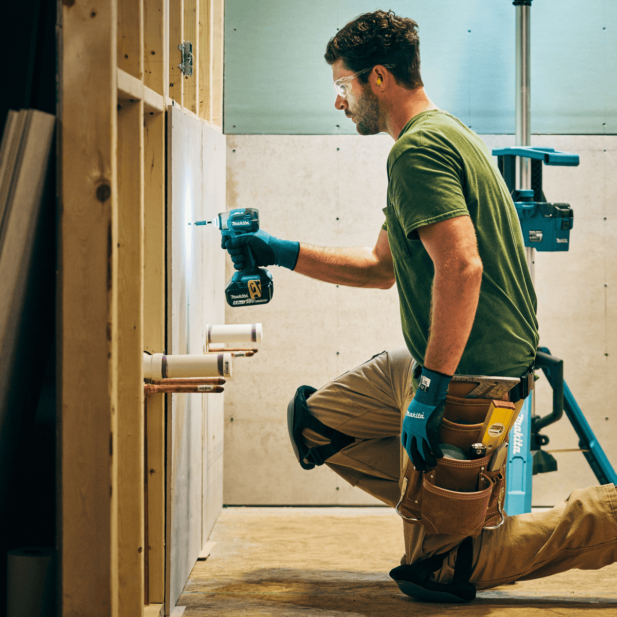 Tradesman kneeling to drive drywall screws into wall backing boards using the compact 18V Makita XDT20 LXT impact driver.
