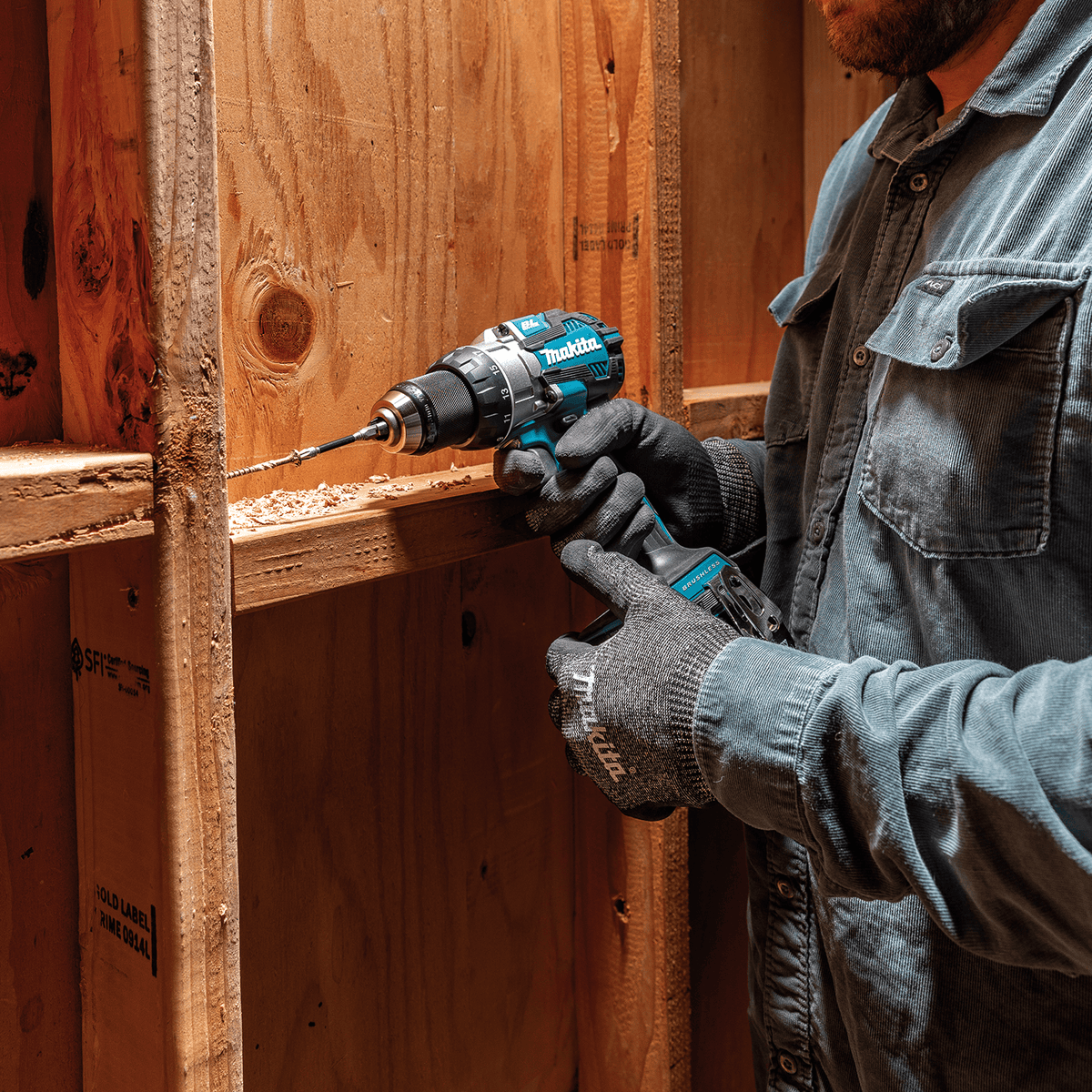 Electrician driving structural fasteners into wall studs using the Makita XFD16Z cordless drill in a tight framing bay.