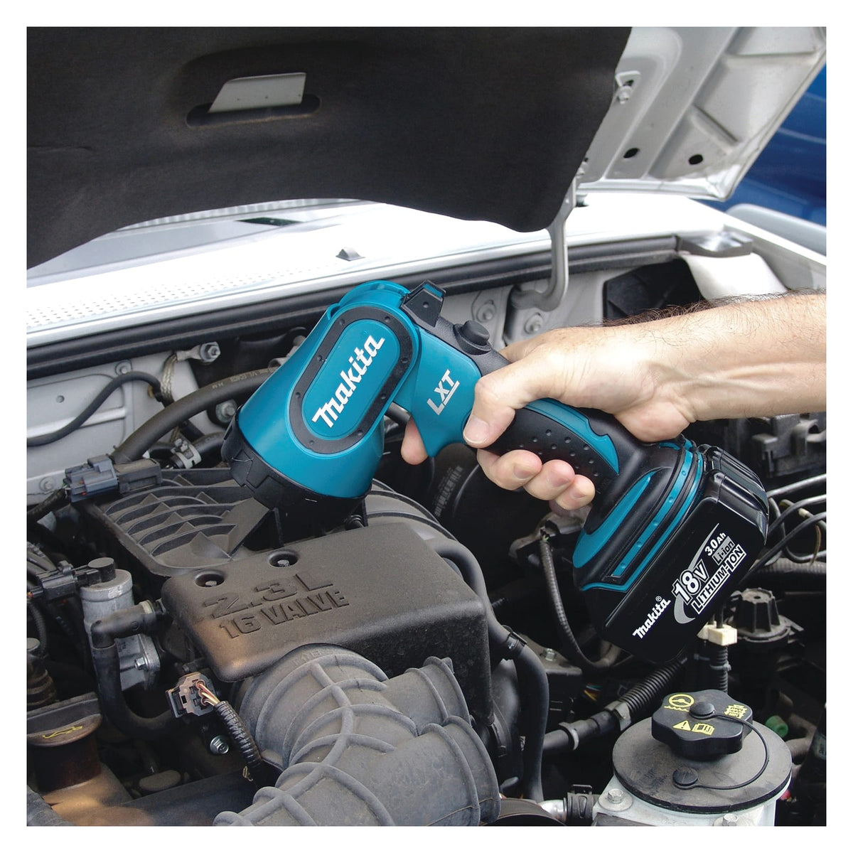Mechanic using the Makita DML185 18V cordless flashlight to illuminate dark automotive engine bay components during repairs.