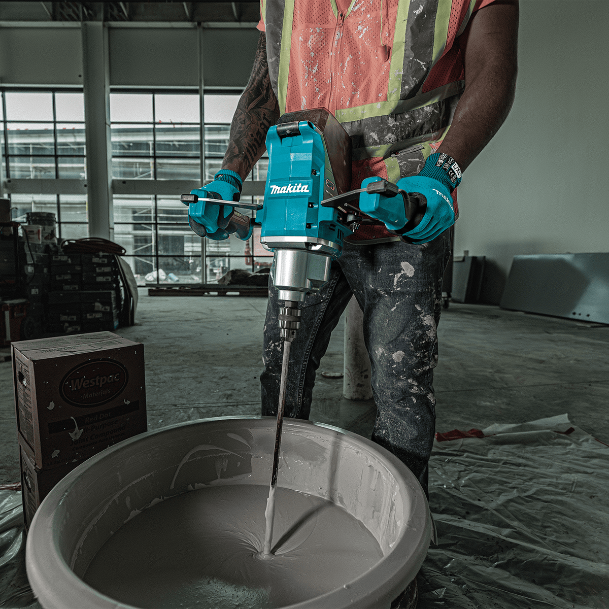 Construction worker holding the Makita 40V max XGT cordless mixer to blend compound in a bucket on a jobsite.