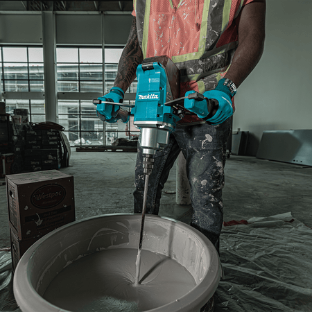 Construction worker holding the Makita 40V max XGT cordless mixer to blend compound in a bucket on a jobsite.