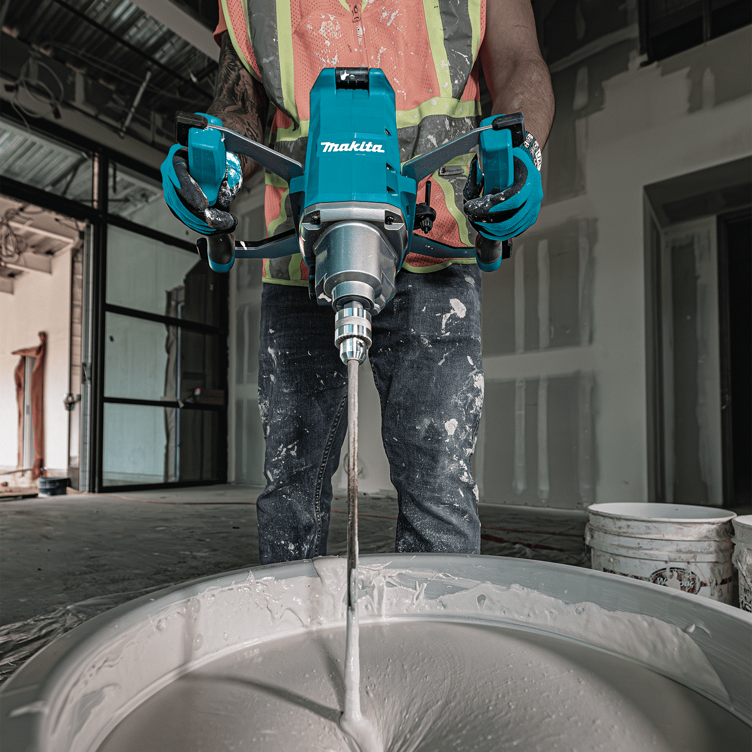 Worker on an indoor jobsite using the Makita 40V XGT cordless mixer to blend drywall mud in a mixing bucket.